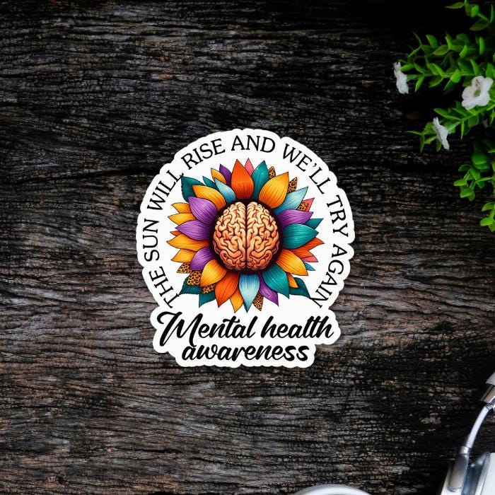 Mental Health Awareness Floral Brain Die Cut Sticker - with vibrant floral colors and white offset and black font. On dark wooden background. Close up.