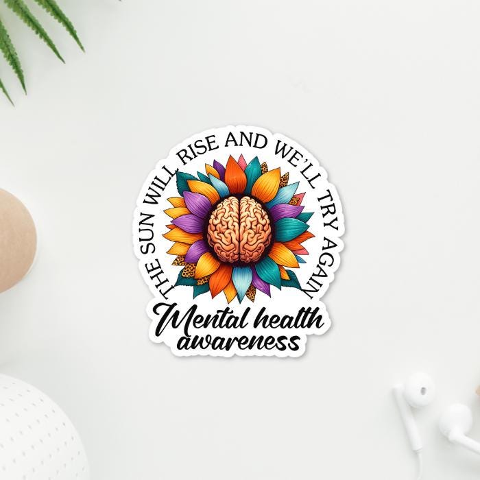 Mental Health Awareness Vibrant Floral Brain Sticker - with inspriational The Sun Will Rise Again Quote. Sticker on white desk with accessories around it. Front View.