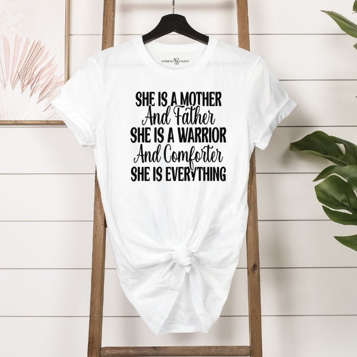 She Is Everything Inspirational White T-shirt for mothers. Short Sleeve with  white bold and cursive font hanging on a ladder front view.