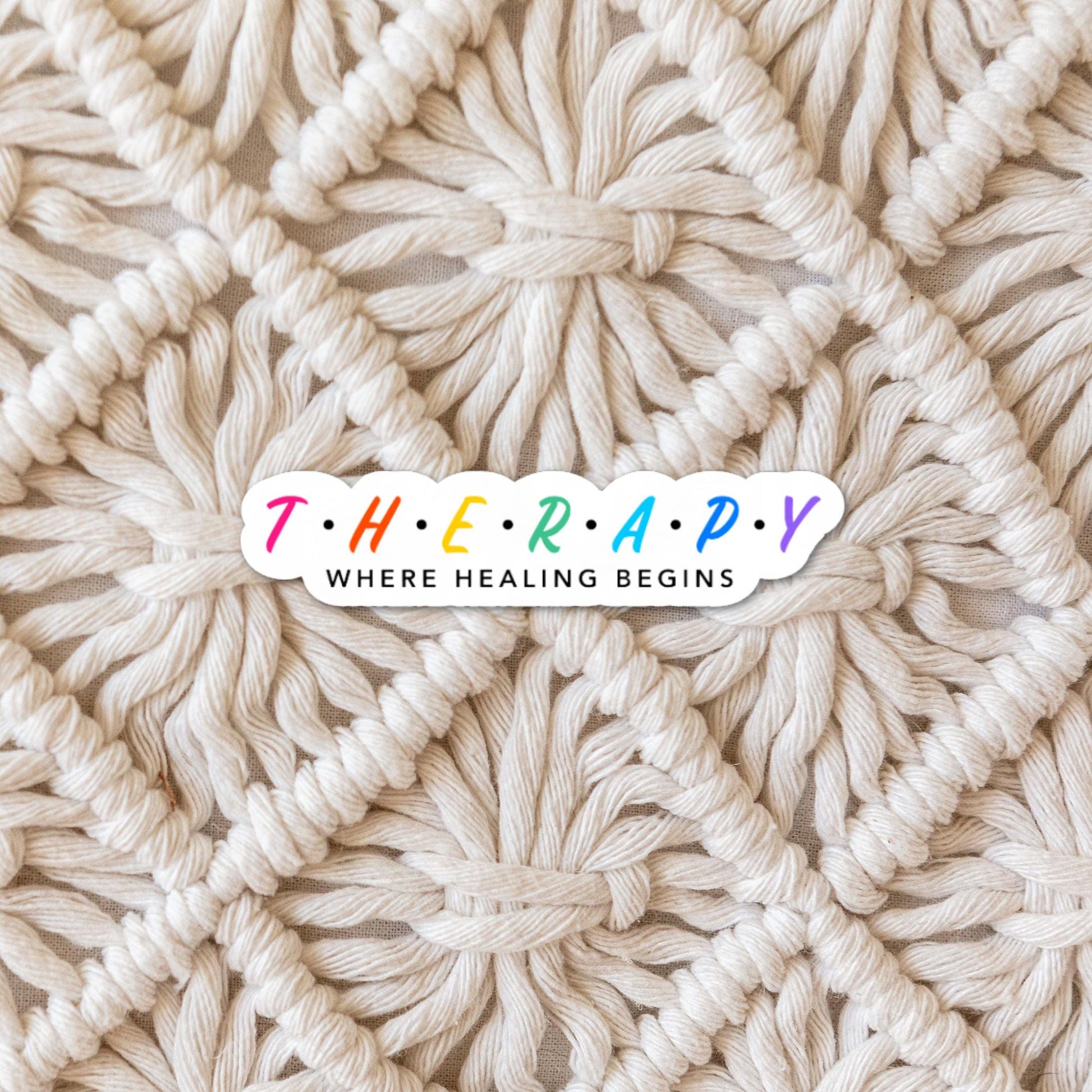 Therapy Where Healing Begins - Inspirational Sticker - Die Cut Sticker with rainbow and black font on tan woven mat background. 
